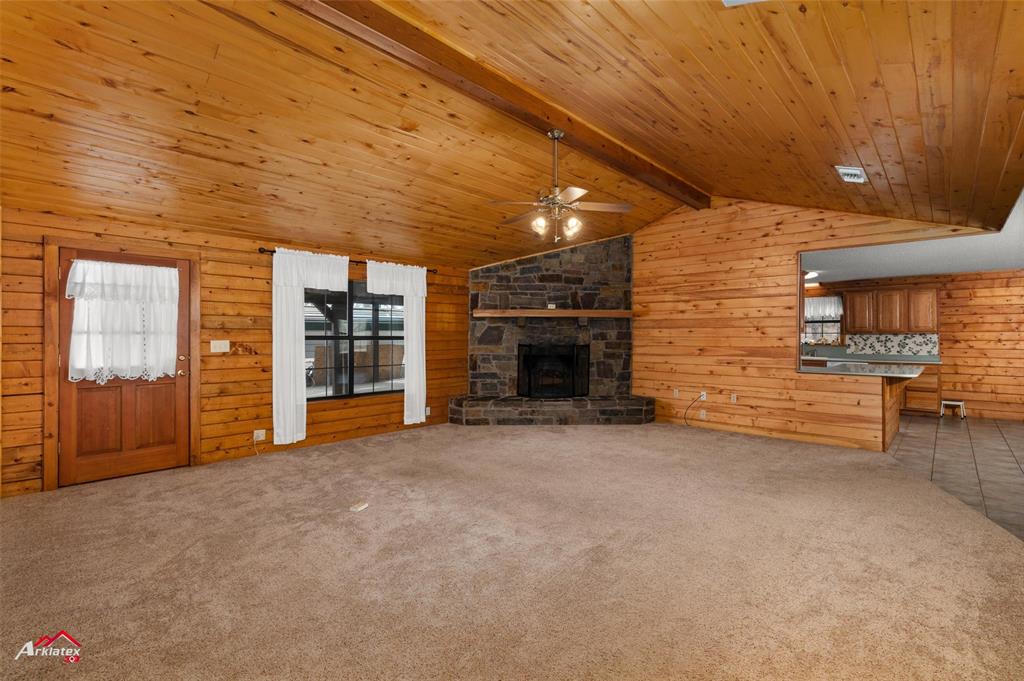 6951 Mira Myrtis Road Ida, LA 71044 - Photo 15 of 32 Unfurnished living room featuring lofted ceiling with beams, wood walls, a stone fireplace, and ceiling fan