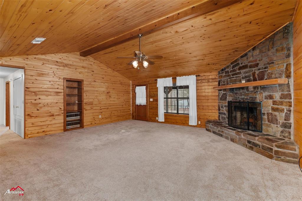 6951 Mira Myrtis Road Ida, LA 71044 - Photo 17 of 32 Unfurnished living room with wooden ceiling, lofted ceiling with beams, wooden walls, a ceiling fan, and a fireplace