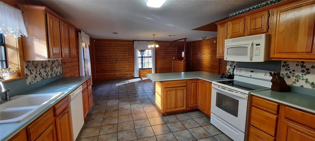 6951 Mira Myrtis Road Ida, LA 71044 - Photo 20 of 32 Kitchen with sink, wood walls, kitchen peninsula, pendant lighting, and white appliances