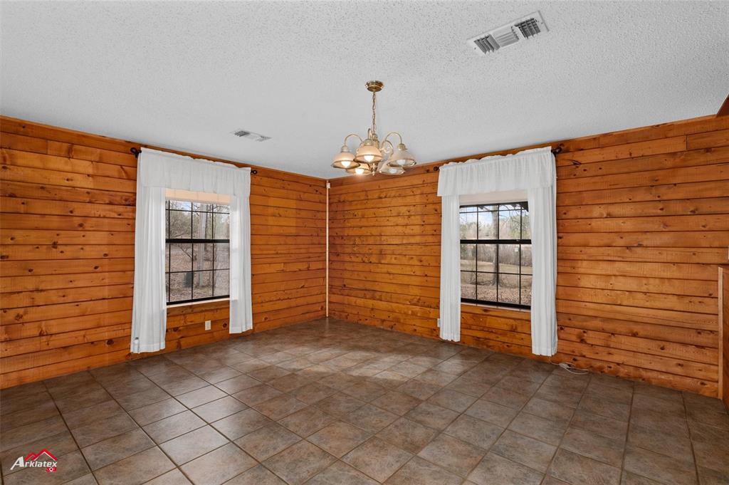 6951 Mira Myrtis Road Ida, LA 71044 - Photo 21 of 32 Spare room with a textured ceiling, visible vents, a notable chandelier, and wood walls
