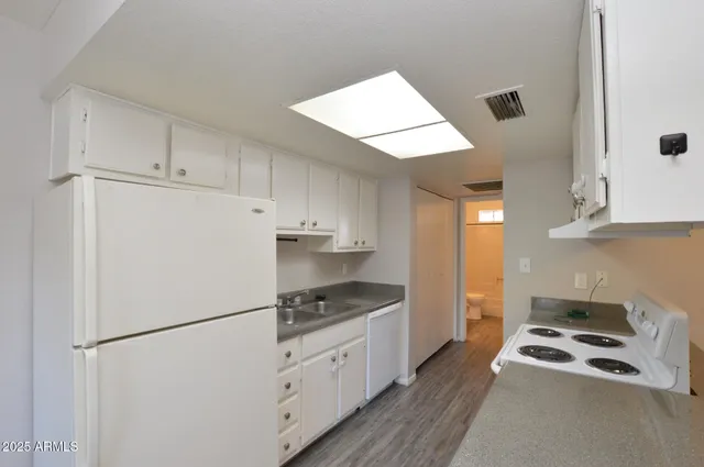 a kitchen with granite countertop a refrigerator a stove a sink and white cabinets with wooden floor