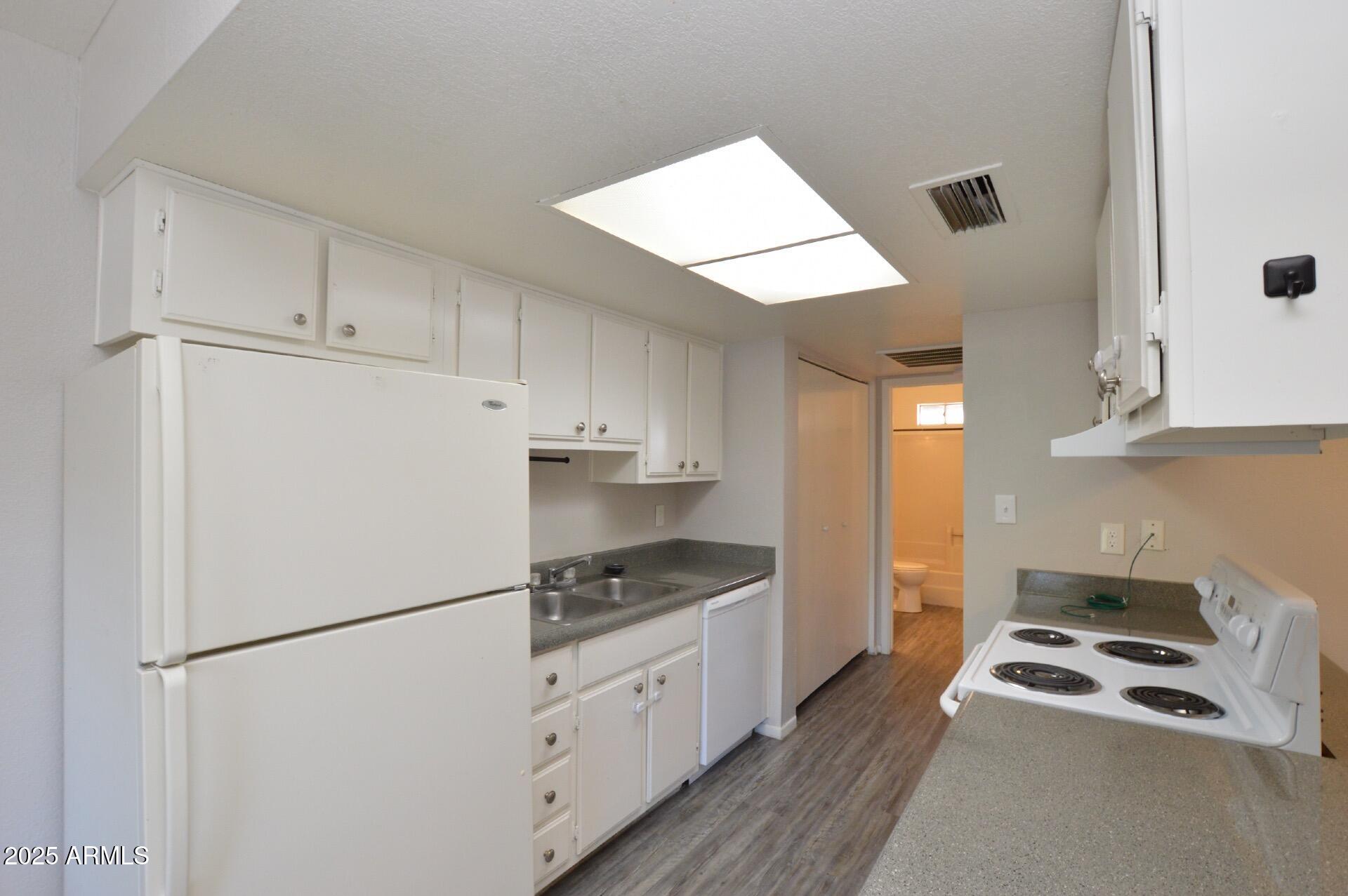 3004 East Waltann Lane, Unit 7 Phoenix, AZ 85032 - Photo 4 of 12 a kitchen with granite countertop a refrigerator a stove a sink and white cabinets with wooden floor