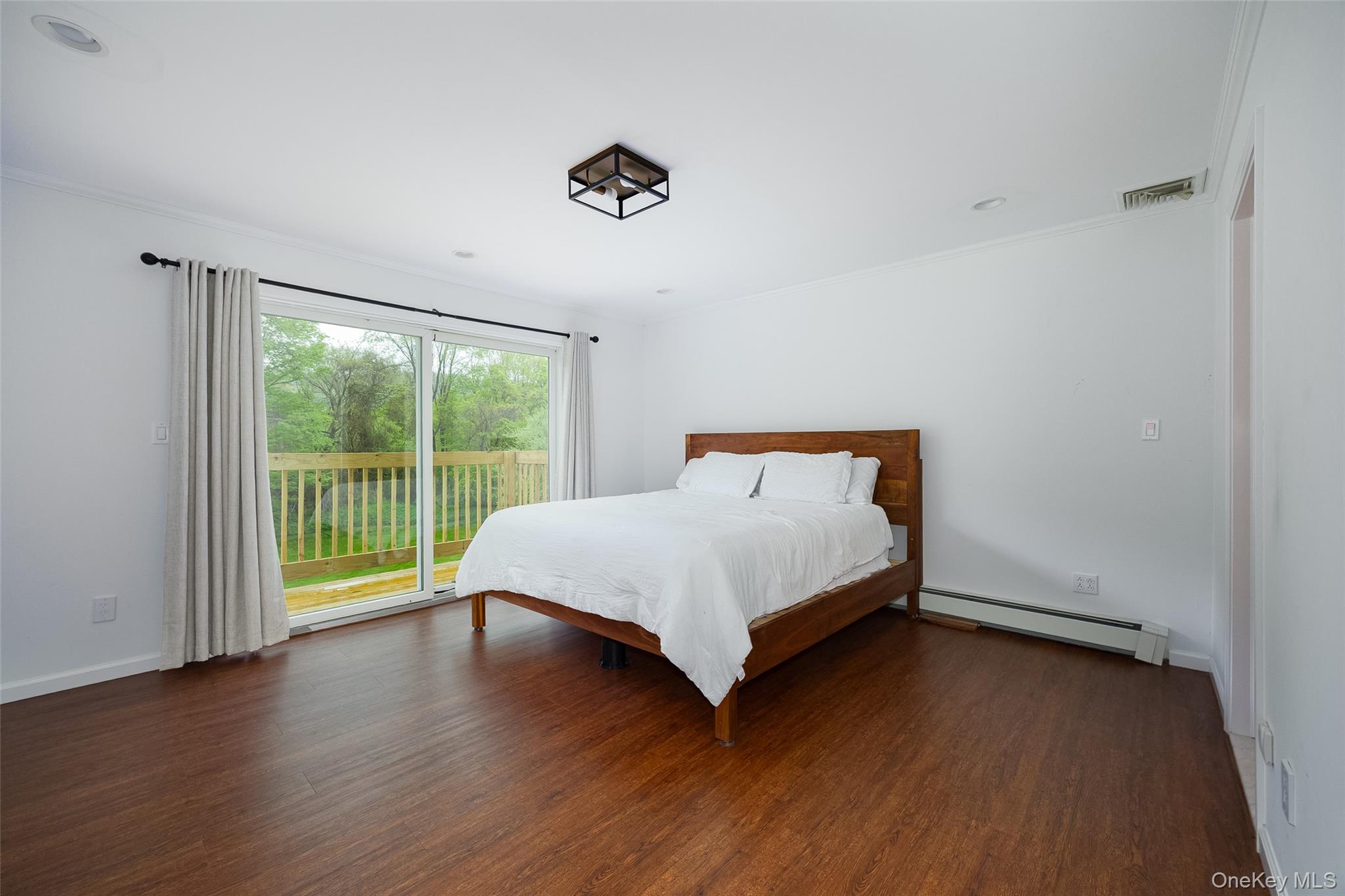 921 West Dover Road Pawling, NY 12564 - Photo 12 of 36 Spacious room with wood-finish flooring, a large sliding glass door opening to an outdoor deck with wood railings, a ceiling-mounted light fixture, and white painted walls