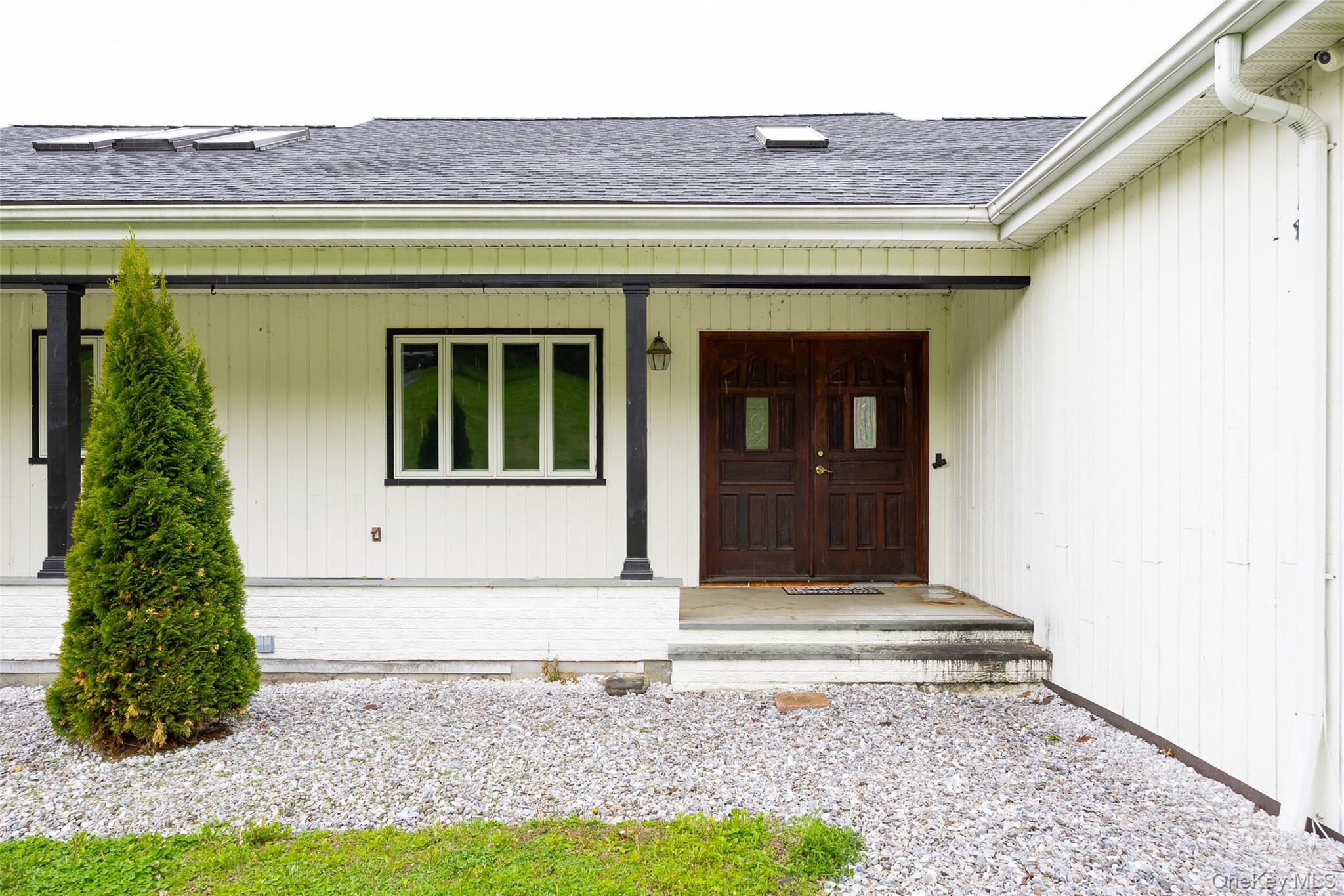 921 West Dover Road Pawling, NY 12564 - Photo 3 of 36 Front entry featuring double dark wood doors with glass inserts, white vertical siding, black support columns, and a dark shingle roof with skylights