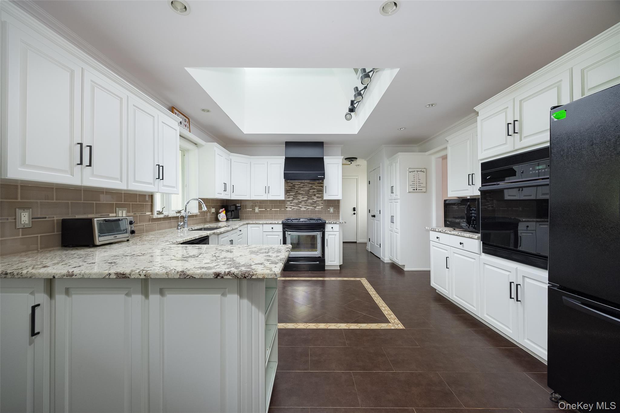 921 West Dover Road Pawling, NY 12564 - Photo 6 of 36 Kitchen featuring white cabinetry, light-toned countertops, a brown subway tile backsplash, dark-finish appliances, and a skylight