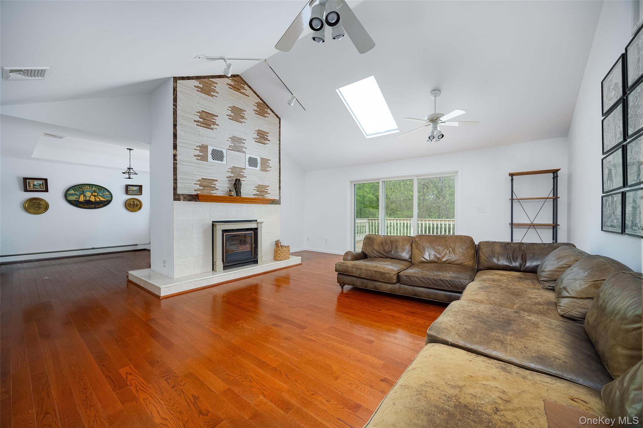 921 West Dover Road Pawling, NY 12564 - Photo 8 of 36 Spacious living area featuring polished wood-finish flooring, a prominent fireplace with a decorative tile surround, vaulted ceilings, and a large skylight