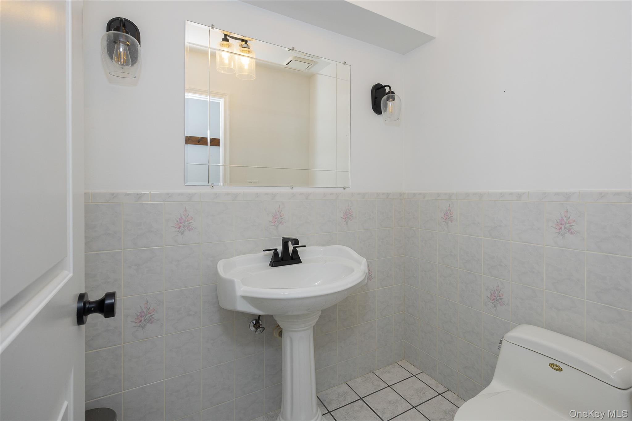 921 West Dover Road Pawling, NY 12564 - Photo 10 of 36 Pedestal sink with a black faucet, white tiled walls with subtle floral accents, and a complementary white toilet