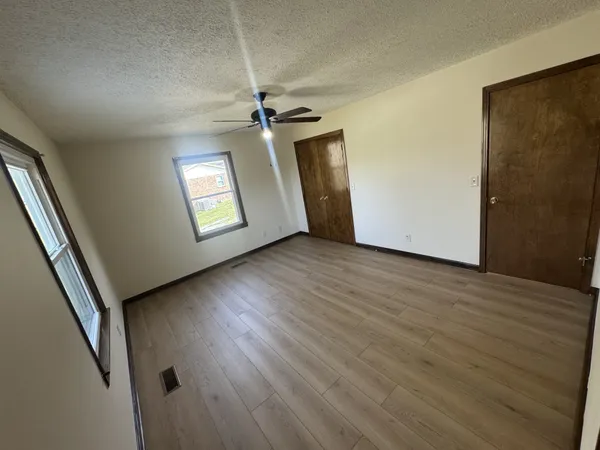 an empty room with wooden floor chandelier fan and windows
