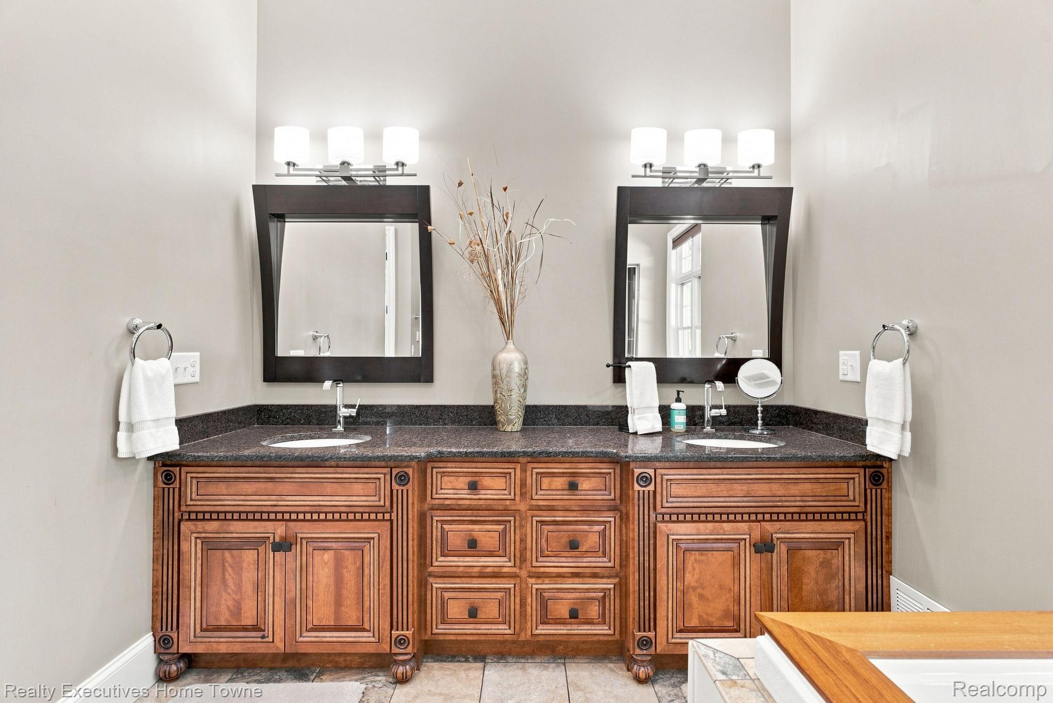 2829 Riverside Drive Port Huron, MI 48060 - Photo 19 of 99 Dual vanity with integrated sinks, dark stone countertop, wood-finish cabinetry, and individual wall-mounted mirrors with overhead lighting