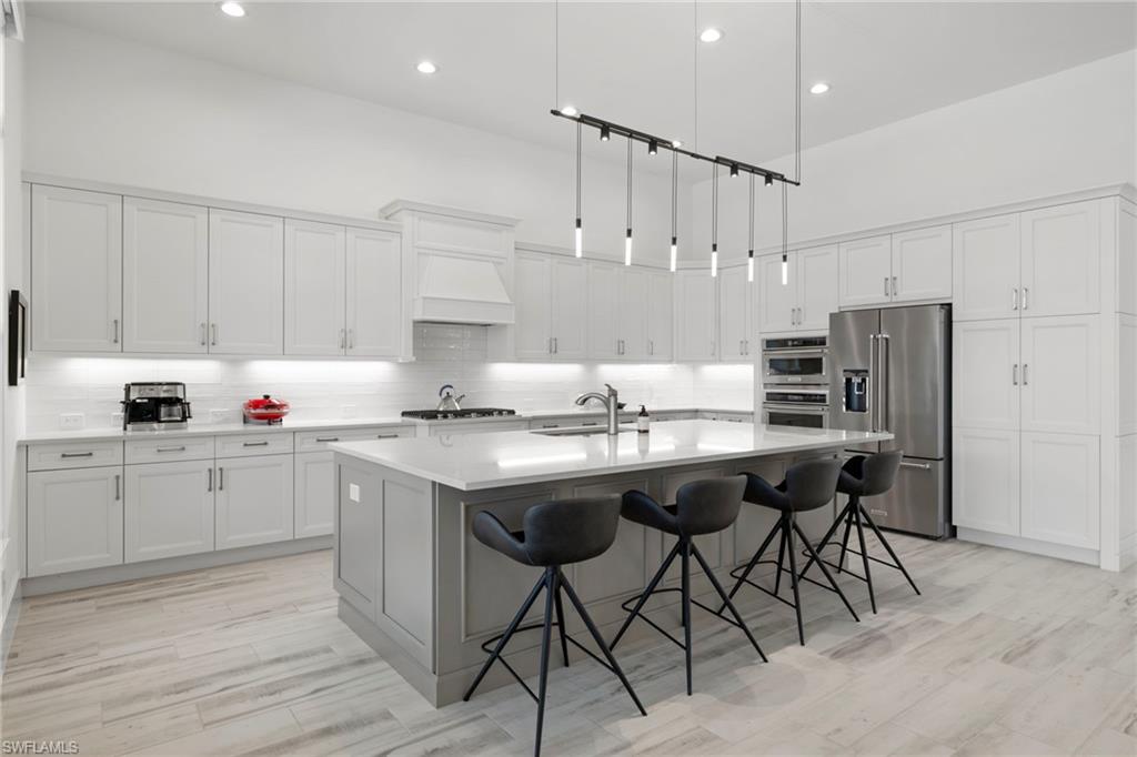 6136 Rodney Bay Lane Naples, FL 34113 - Photo 7 of 29 a kitchen with stainless steel appliances granite countertop a sink a stove a refrigerator and island with wooden floor