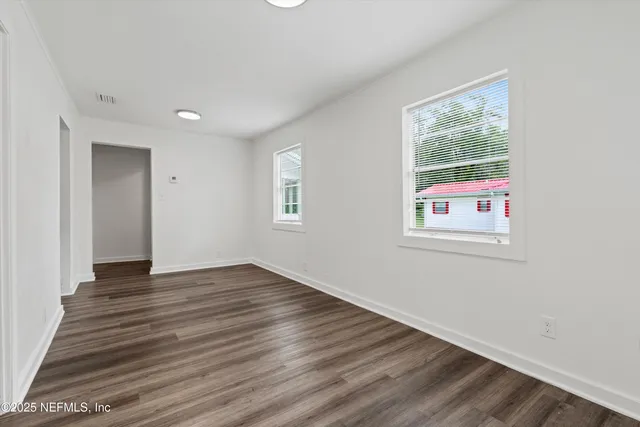 a view of an empty room with wooden floor and a window