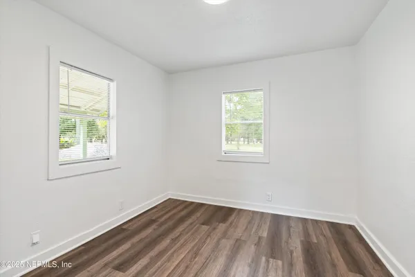 an empty room with wooden floor closet and windows
