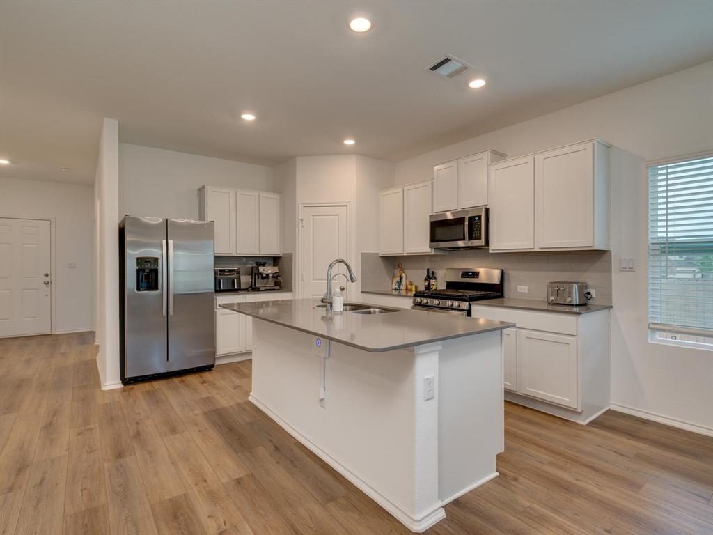 1208 Sweetspire Street Leander, TX 78641 - Photo 2 of 36 Modern kitchen featuring an island with a sink, white cabinetry, stainless steel appliances, wood-finish flooring, and recessed lighting