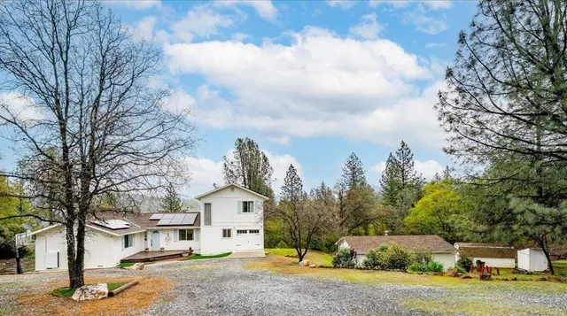a view of a white house next to a yard with big trees