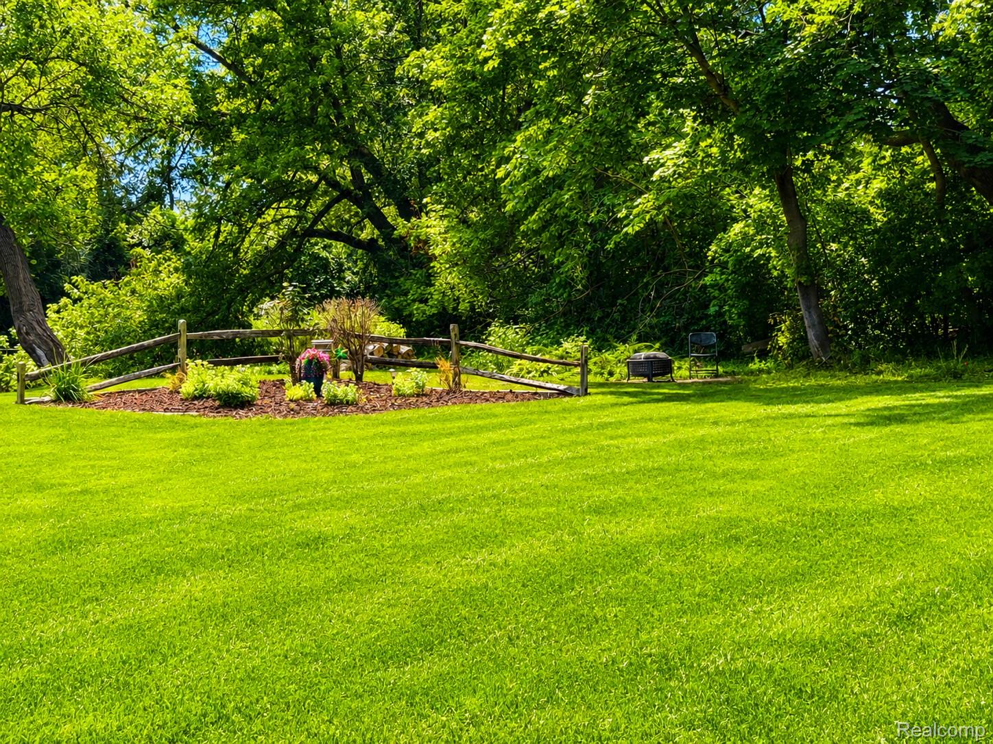 2495 North Custer Road Monroe, MI 48162 - Photo 43 of 44 Expansive green lawn surrounded by mature trees, featuring a decorative flower bed with a rustic wooden fence