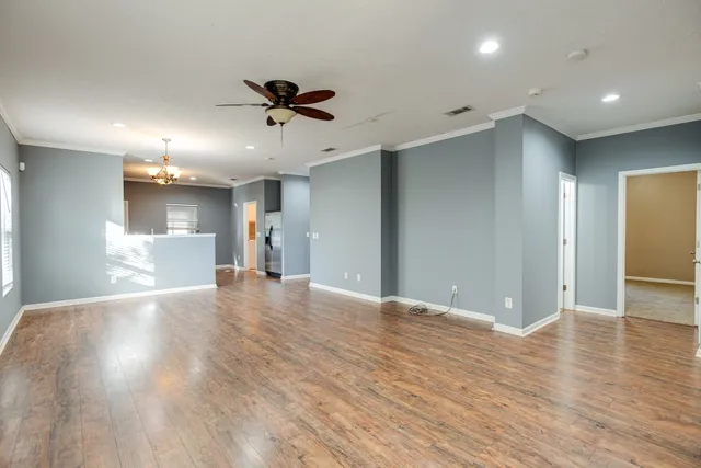 a view of an empty room with wooden floor and a ceiling fan