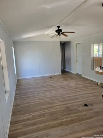 a view of an empty room with wooden floor and a ceiling fan