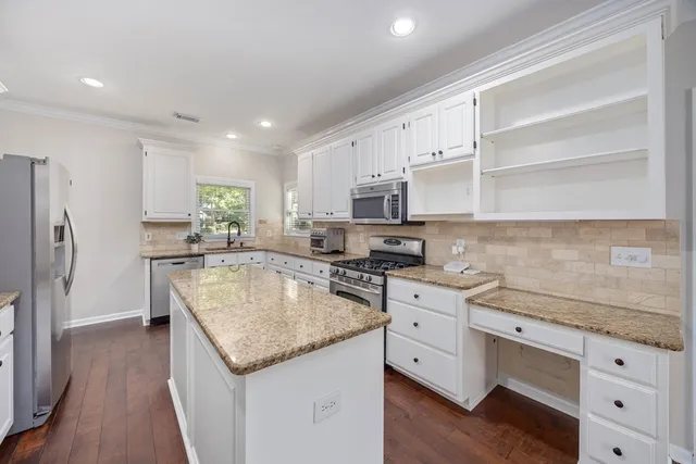 a kitchen with stainless steel appliances granite countertop a sink dishwasher a refrigerator and white cabinets with wooden floor