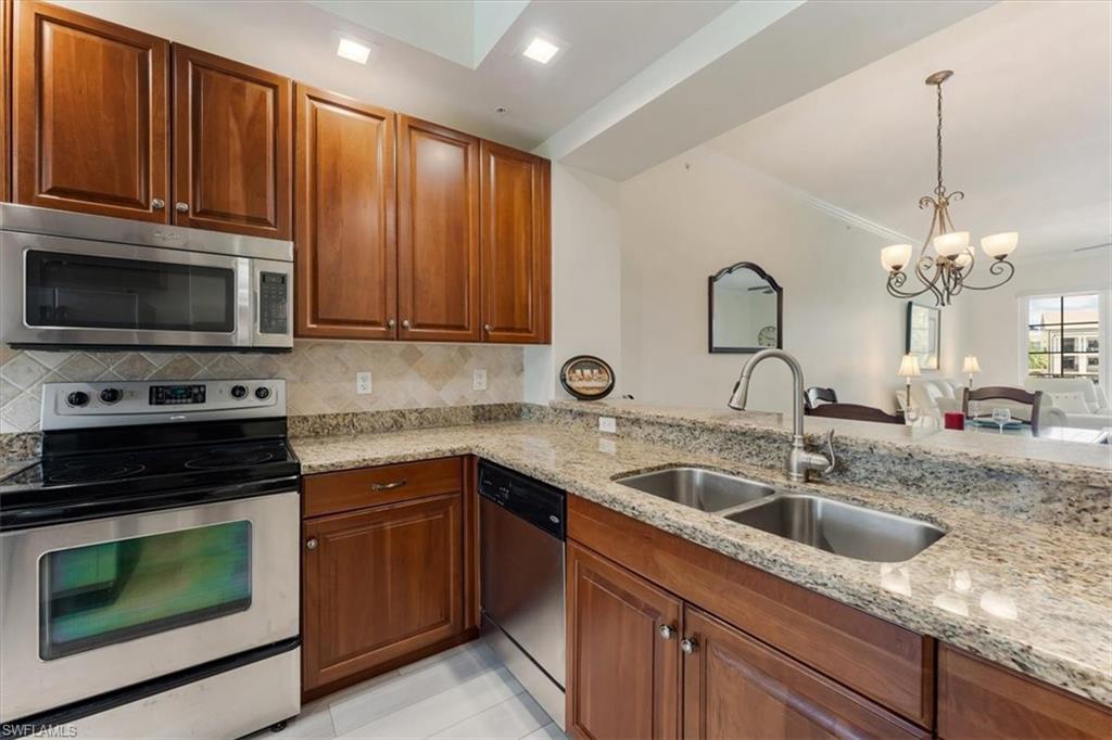 5080 Annunciation Circle, Unit 204 Ave Maria, FL 34142 - Photo 9 of 24 a kitchen with stainless steel appliances granite countertop a sink dishwasher stove and microwave with wooden cabinets