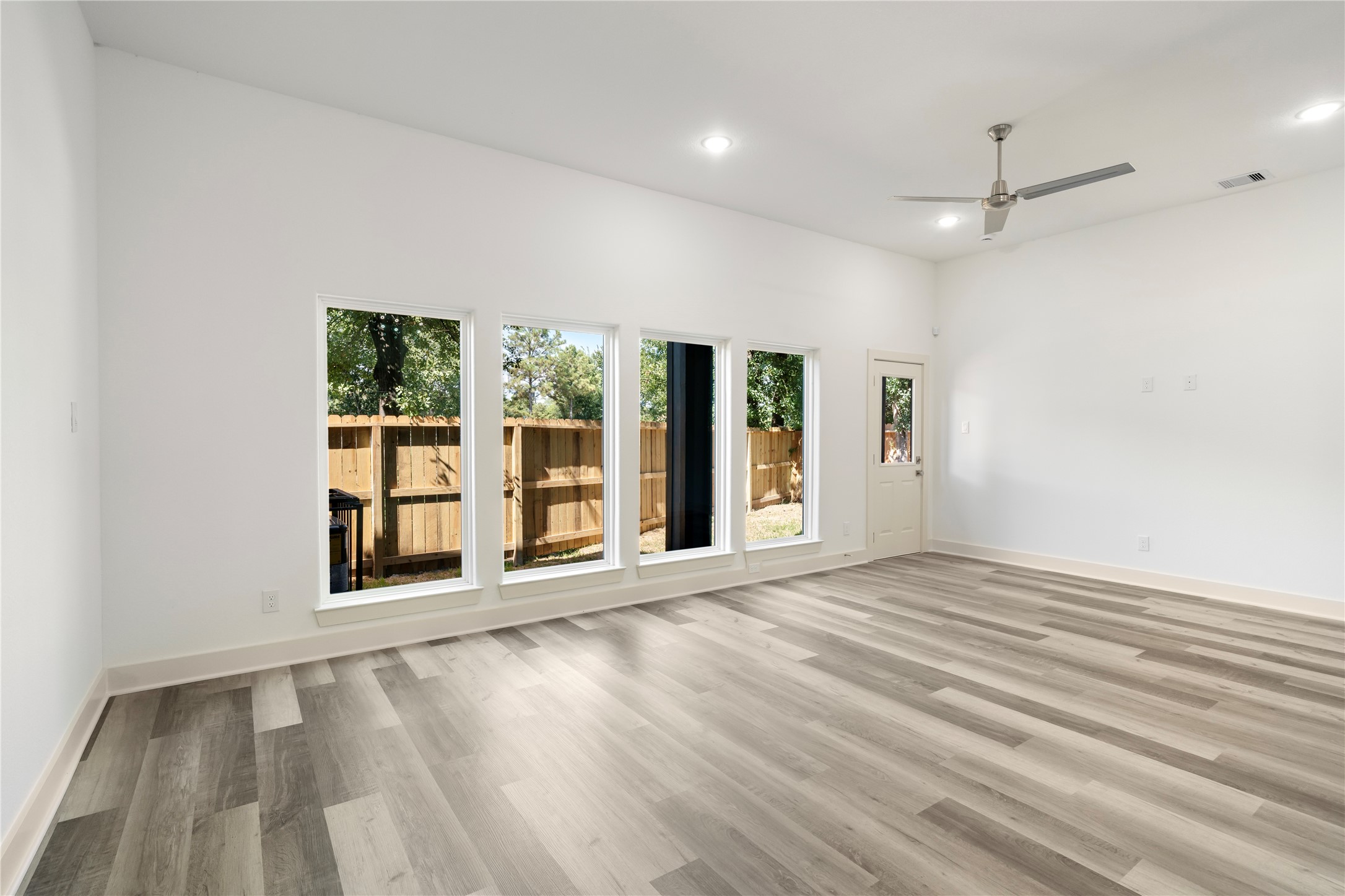 5629 Malmedy Road Houston, TX 77033 - Photo 18 of 24 Bright and spacious living room with large windows, modern gray flooring, and a ceiling fan, offering a seamless connection to the outdoors through a glass door.