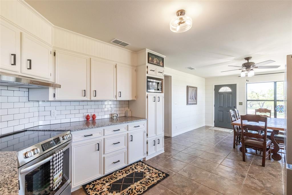 642 Fm 3200 Comanche, TX 76442 - Photo 8 of 37 a kitchen with stainless steel appliances granite countertop a stove top oven a sink a dining table and chairs with white cabinets