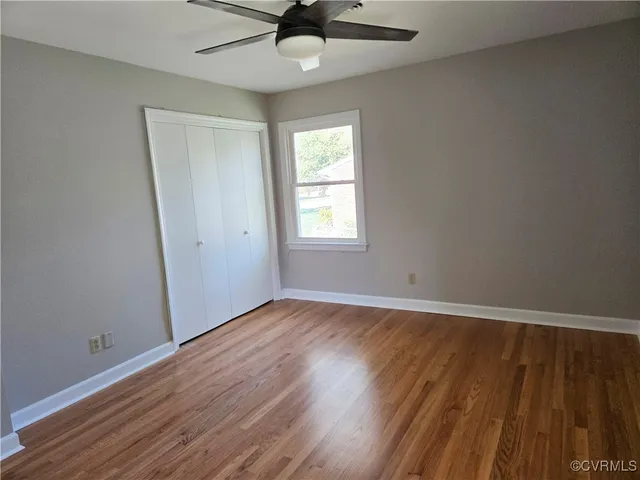 an empty room with wooden floor fan and windows