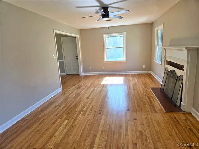 an empty room with wooden floor a ceiling fan and windows