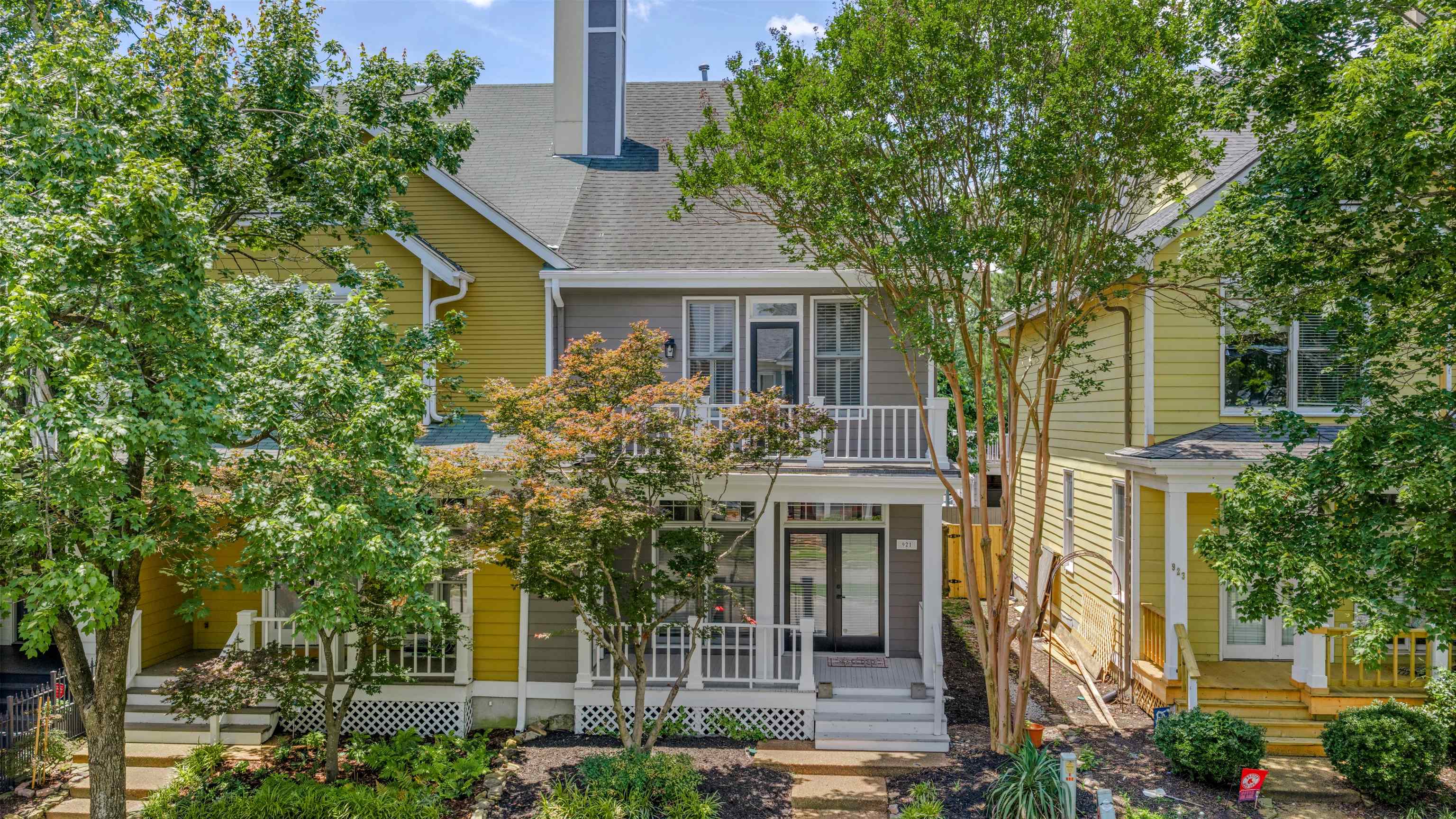 921 Harbor View Drive Memphis, TN 38103 - Photo 22 of 33 Townhome exterior featuring a prominent second-story balcony with white railing, a ground-level porch with white railing, a dark entry door with transom window, light gray siding, and surrounding mature trees and shrubbery
