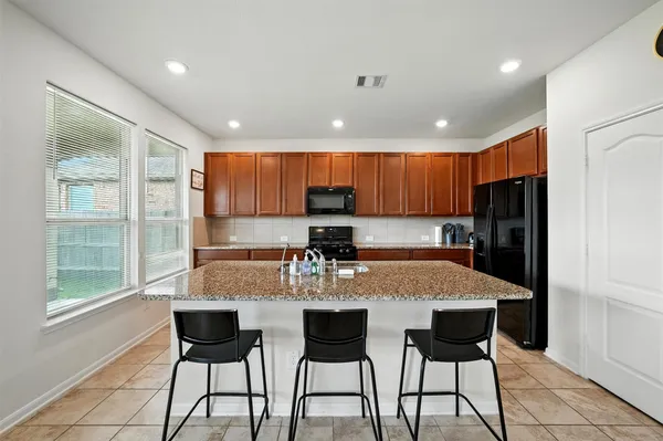 a kitchen with granite countertop a refrigerator and chairs