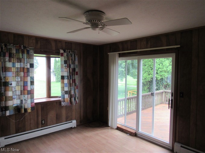 2189 Sentinel Road Dorset, OH 44032 - Photo 9 of 28 Unfurnished room with a baseboard radiator, a wealth of natural light, wood walls, light hardwood floors, and ceiling fan