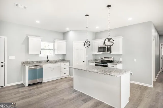 a large kitchen with stainless steel appliances granite countertop a stove a sink a center island a sink and a wooden floor