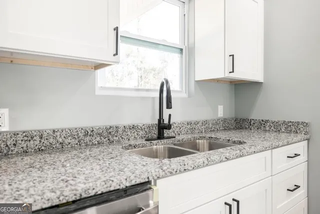 a kitchen with granite countertop a sink and a white wooden cabinets