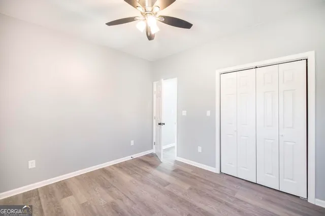 an empty room with wooden floor closet and fan