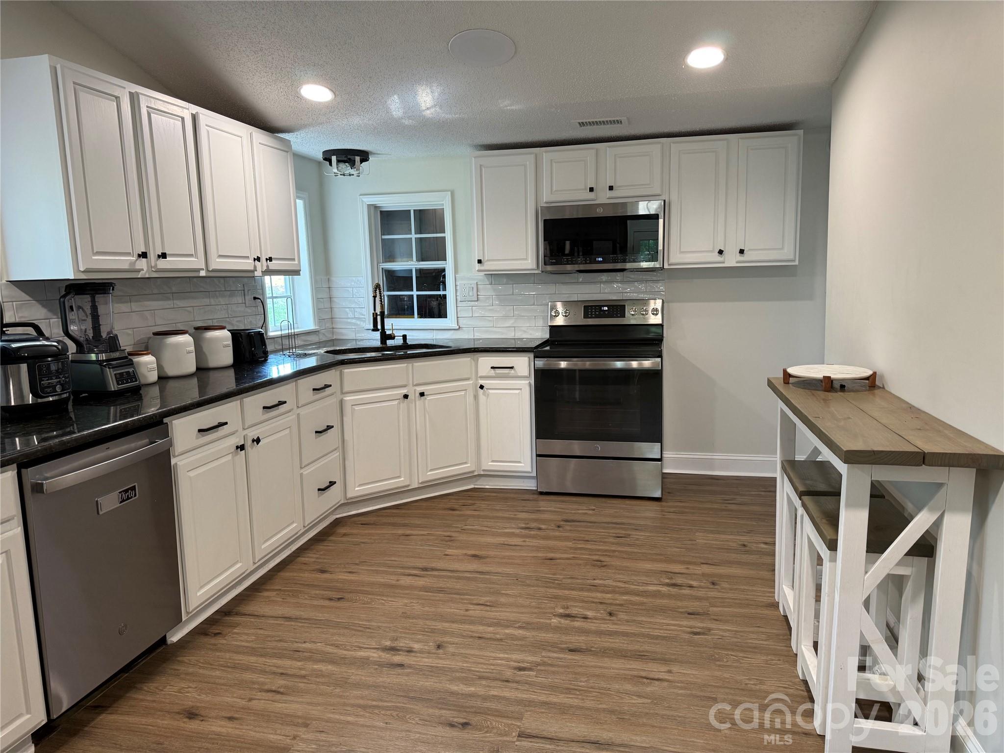 1442 Lee Pearson Road Granite Falls, NC 28630 - Photo 10 of 40 a kitchen with granite countertop a stove top oven a sink dishwasher and a refrigerator with wooden floor