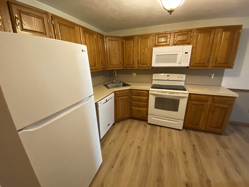 501 Ridgefield Circle, Unit B Clinton, MA 01510 - Photo 3 of 17 a kitchen with wooden floor sink and white stainless steel appliances