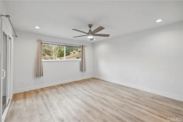 an empty room with wooden floor chandelier fan and windows