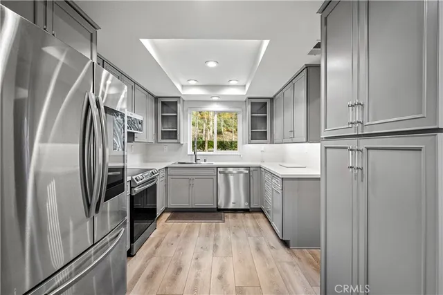 a kitchen with stainless steel appliances granite countertop a refrigerator a sink dishwasher a stove and white countertops with wooden floor