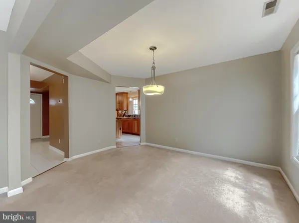 an empty room with chandelier fan and kitchen view