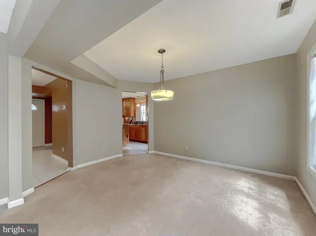 an empty room with chandelier fan and kitchen view