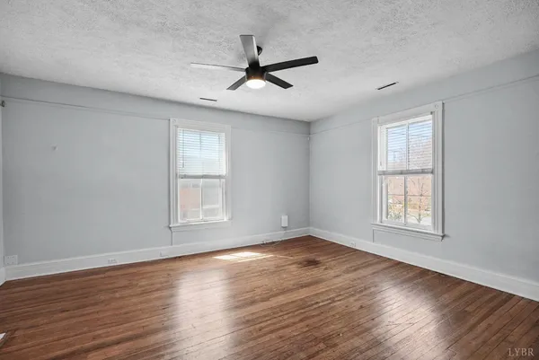 an empty room with wooden floor fan and windows