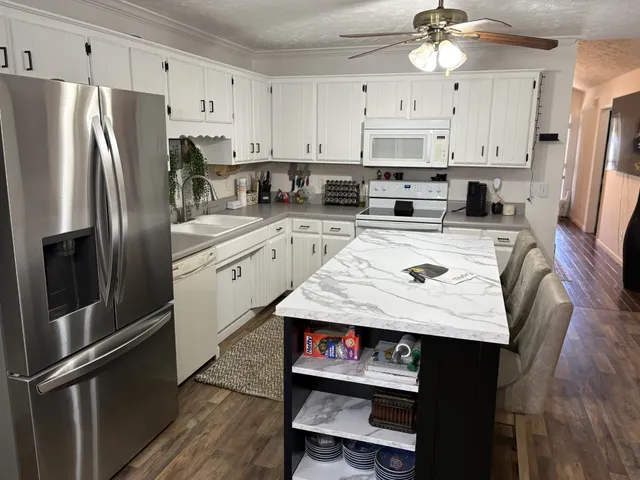 a kitchen with stainless steel appliances granite countertop a refrigerator a stove a sink dishwasher and white cabinets with wooden floor