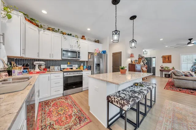 a kitchen with stainless steel appliances kitchen island granite countertop a stove top oven a sink a dining table and chairs with the wooden floor