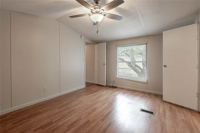 an empty room with wooden floor chandelier fan and windows