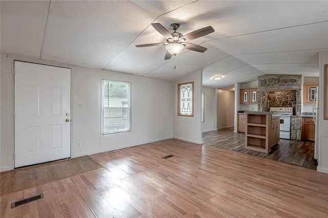 an empty room with wooden floor fan and windows