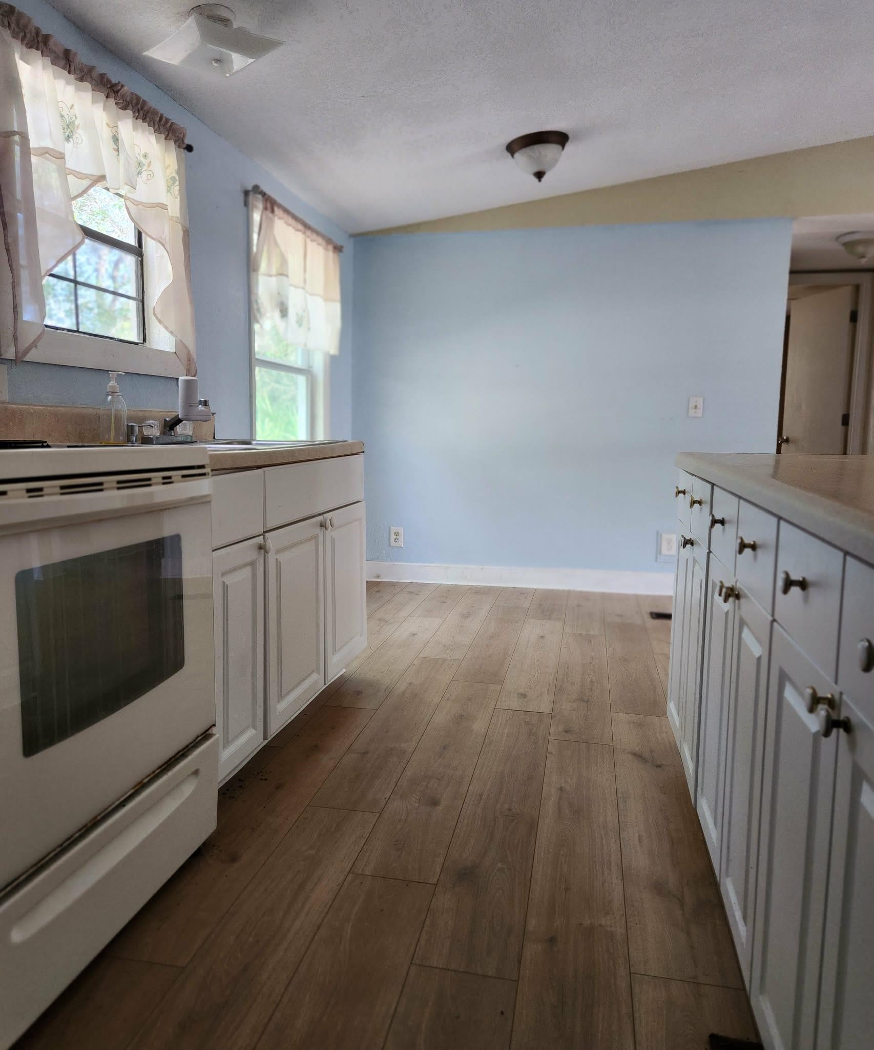 890 Poinsettia Road, Unit B St. Augustine, FL 32086 - Photo 8 of 14 Kitchen featuring white range with electric stovetop, white cabinets, light wood-style floors, light countertops, and a textured ceiling