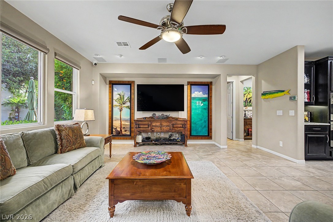 7415 Campbell Ranch Avenue Las Vegas, NV 89179 - Photo 13 of 52 Natural light bathes this spacious living room, featuring a classic ceiling fan and elegant tiled flooring.