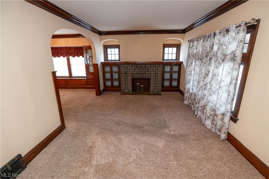 10105 Unity Avenue Cleveland, OH 44111 - Photo 5 of 35 Unfurnished living room with light colored carpet, a healthy amount of sunlight, crown molding, and a brick fireplace