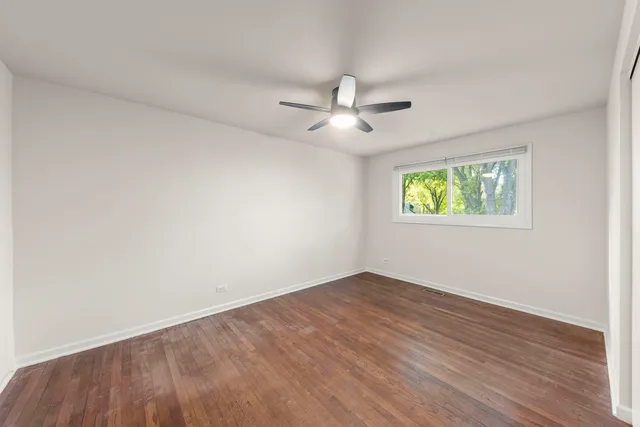 an empty room with wooden floor ceiling fan and windows