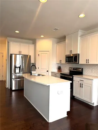 a kitchen with stainless steel appliances kitchen island granite countertop a stove top oven a sink a refrigerator with white cabinets and wooden floor