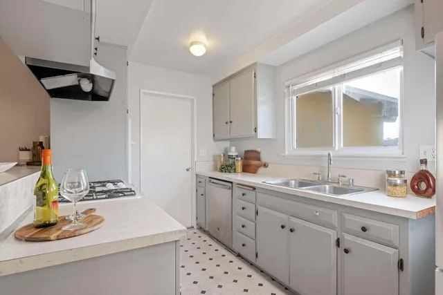a kitchen with a sink dishwasher and white cabinets with wooden floor
